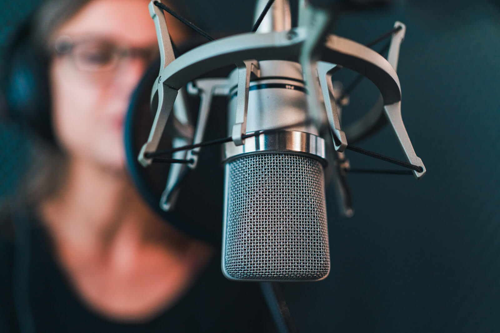 Studiomikrofon im Tonstudio der audiomarketeers, im Hintergrund eine Sprecherin mit Kopfhörern